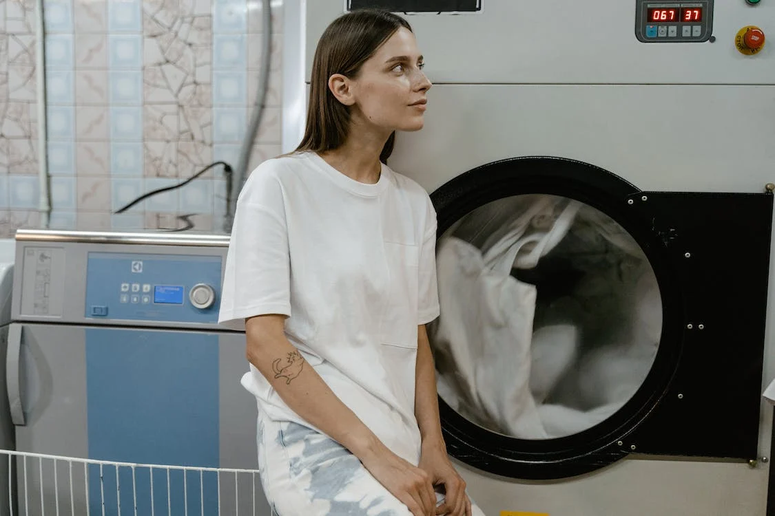 A woman sitting in front of a washing machine, utilizing a laundry service.