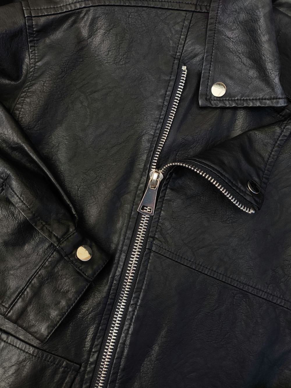 Close-up of a black leather jacket featuring a silver zipper, snap buttons, and visible stitching details.